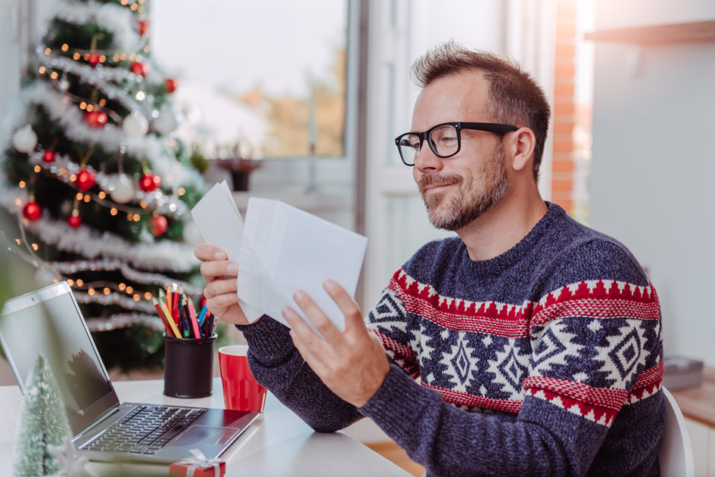 Men wearing blue sweater and eyeglasses opening christmas letter
