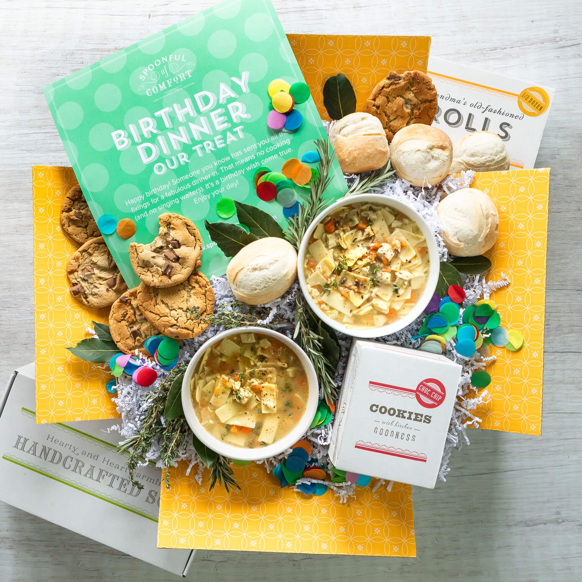 Birthday Care Package, Two bowls of chicken noodle soup surrounded by rolls and cookies and colorful confetti. Insert in image reads: Birthday Dinner our Treat